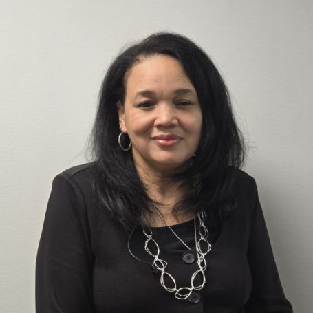 A woman with shoulder-length dark hair wearing a black top and silver necklace, and smiling.